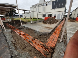 A dug trench with orange electrical conduits buried in the ground.