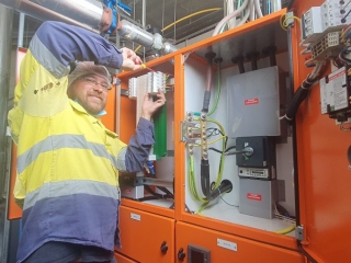 An electrician wearing a yellow safety vest working on an electrical panel.