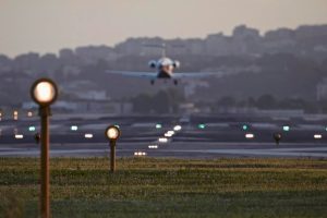 A jet airplane is landing on a runway with airfield ground lights in the background.