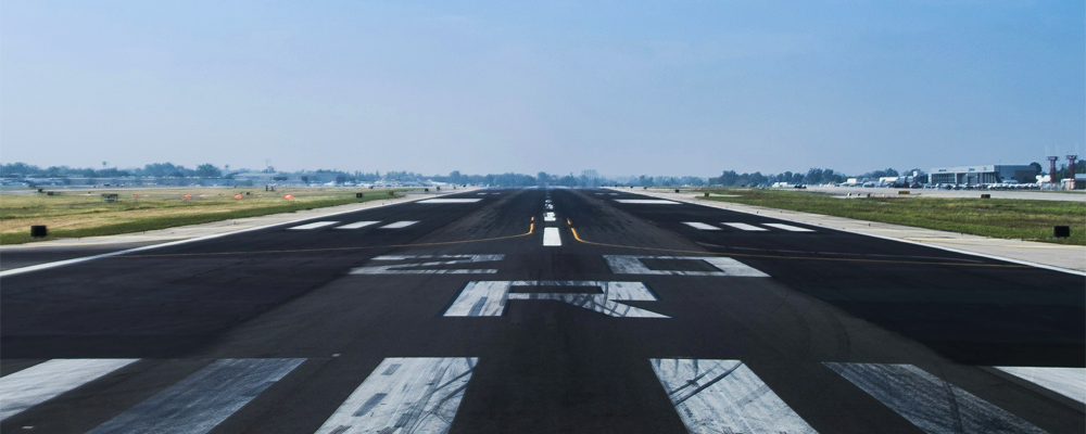 Daytime View of Runway Markings and Airfield Lighting Infrastructure A ground-level view down the center of an empty airport runway, showing the white painted markings and the edges where airfield lighting systems are installed.