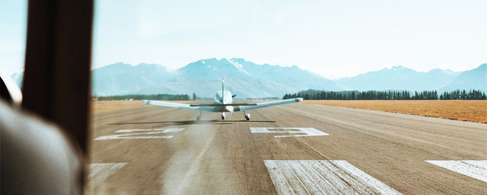 A small propeller plane taking off from a rural airfield runway, which relies on visual markings by day and airfield lighting by night.