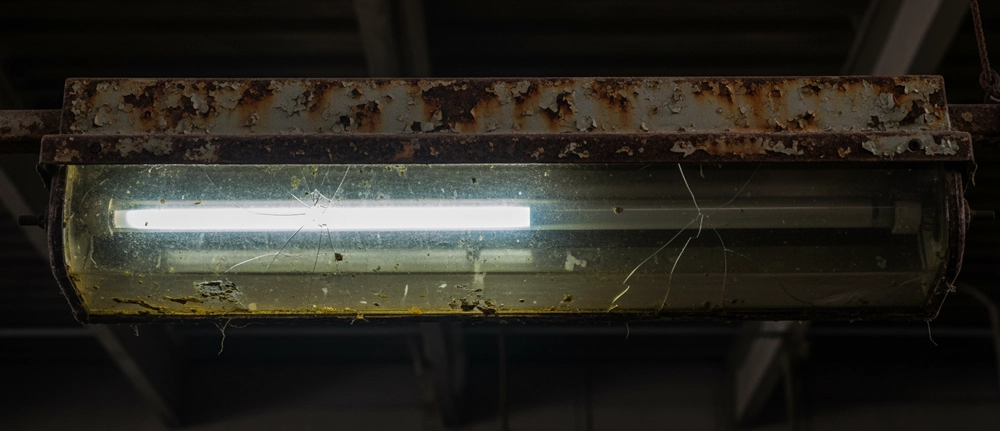 Ageing Industrial Lighting Fitting Needing Replacement Corroded industrial light fitting with a cracked cover and visible wear in a warehouse setting